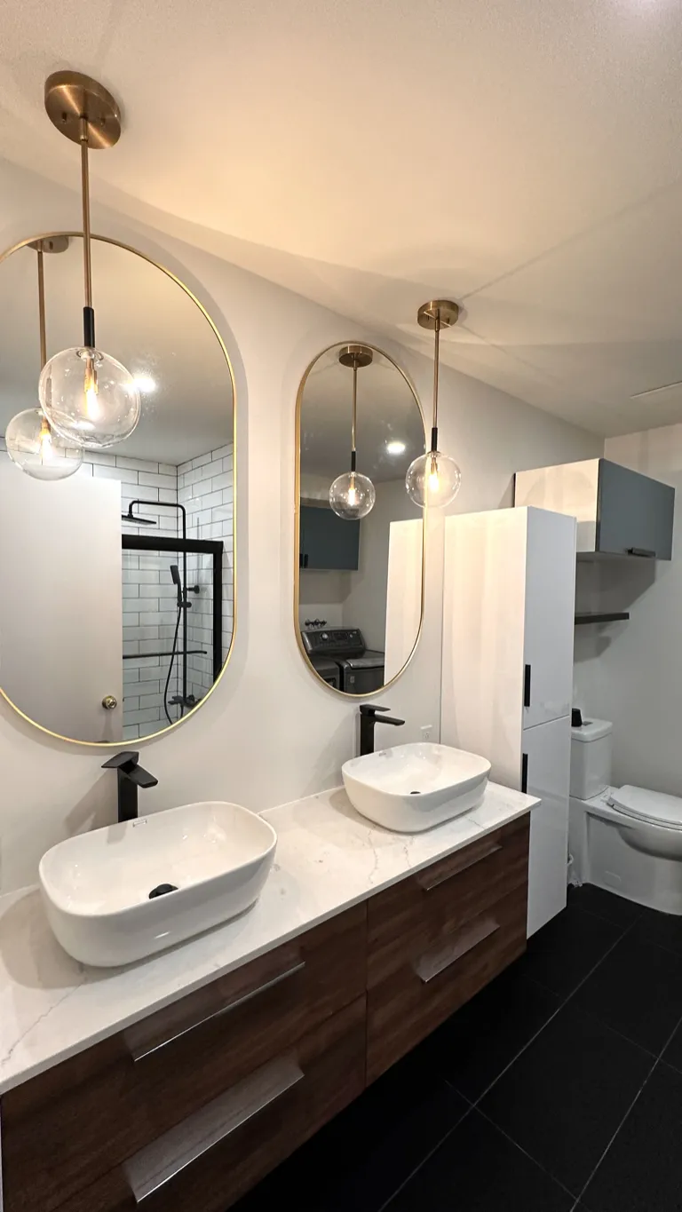 Salle de bain rénovée avec double vasque, miroirs dorés et vanité en noyer